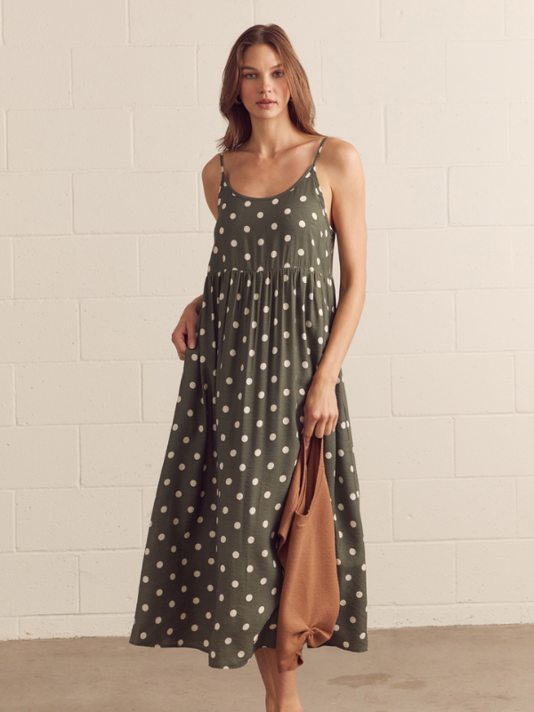 Woman wearing a green polka dot dress with a brown bag against a beige brick wall.