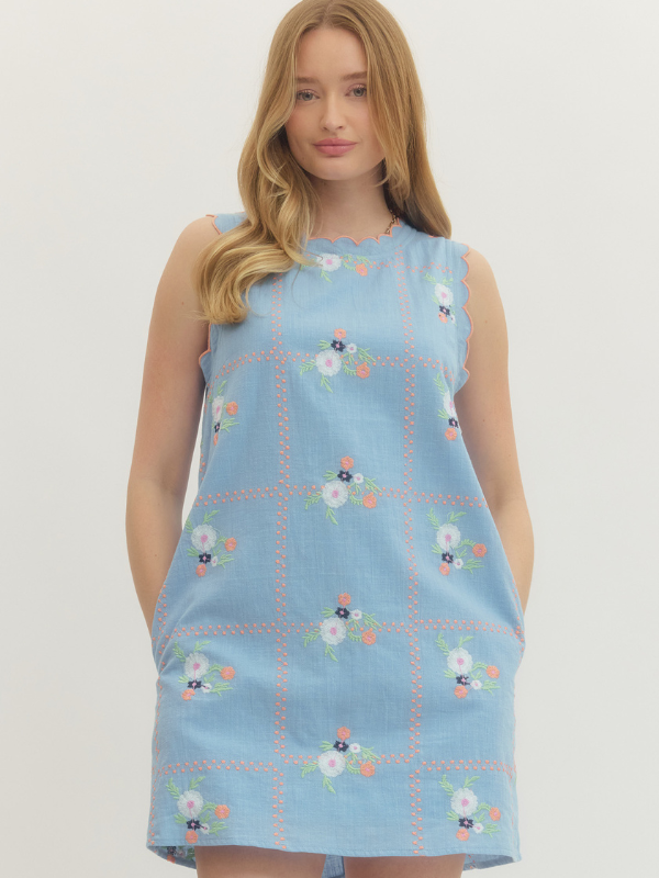 Woman wearing a light blue sleeveless dress with floral patterns on a plain background
