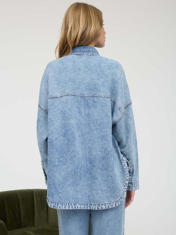 Person wearing a light blue denim jacket and jeans on a plain background