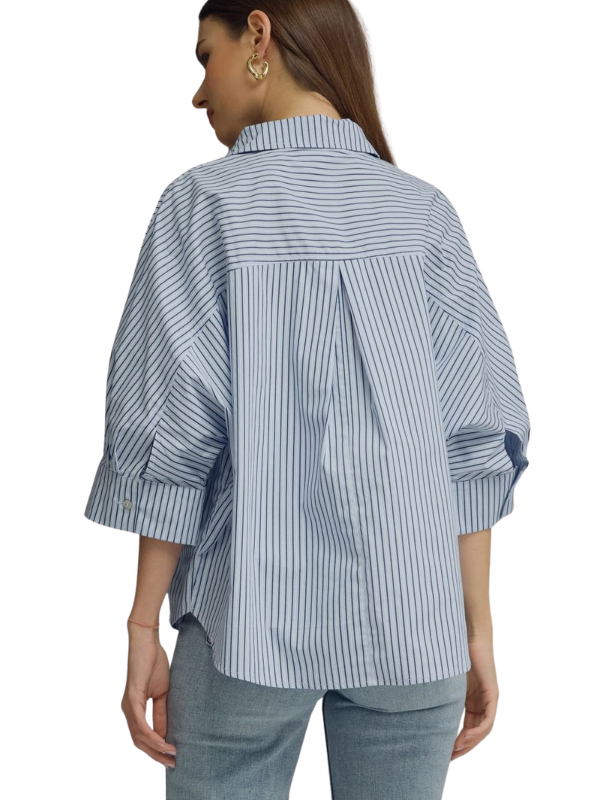 A woman shown from the back wearing a light blue and white vertically striped button-up shirt with three-quarter sleeves and light-wash jeans, against a plain white background.