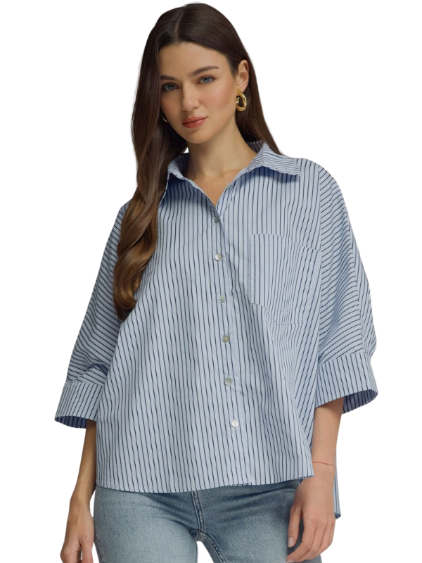 A woman modeling an oversized blue and white vertically striped button-up shirt with three-quarter sleeves, paired with light-wash jeans against a plain white background.