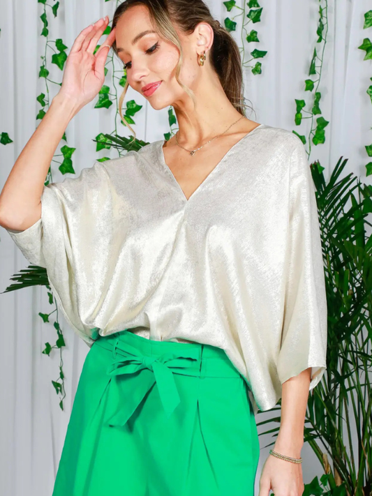 Woman wearing a white top and green pants with a leafy background