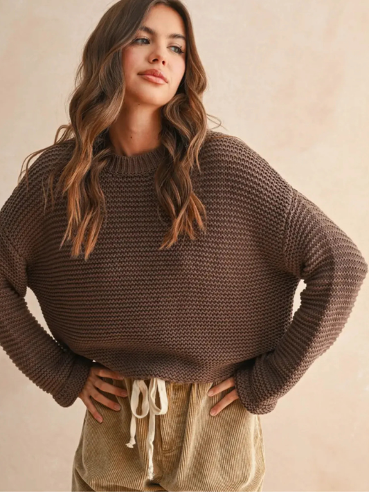 Woman wearing a brown knitted sweater and beige pants against a beige background