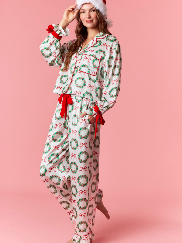 Woman wearing festive pajamas with wreath and bow pattern on a pink background