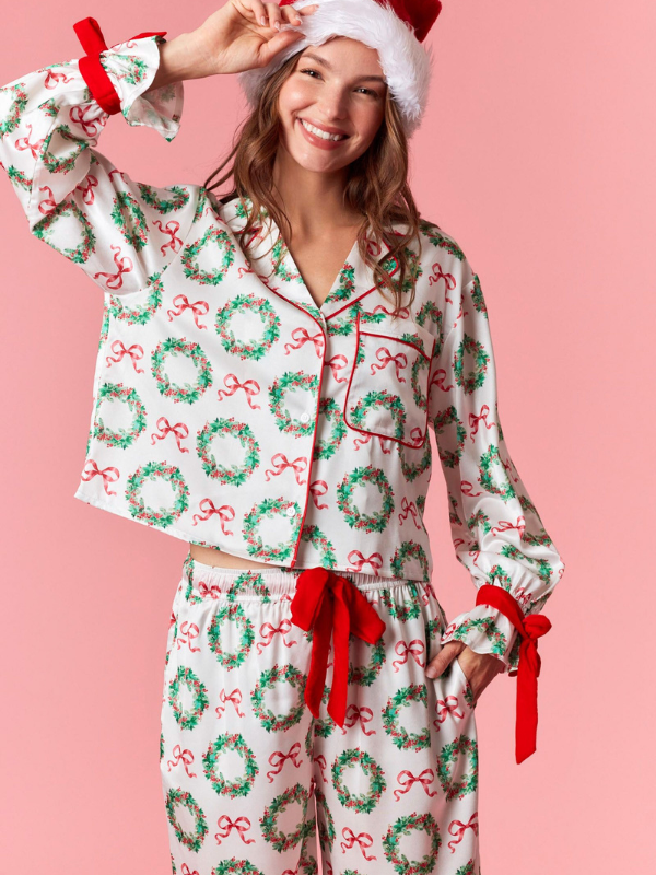 Woman wearing a Christmas-themed pajama set with wreaths and red bows on a pink background