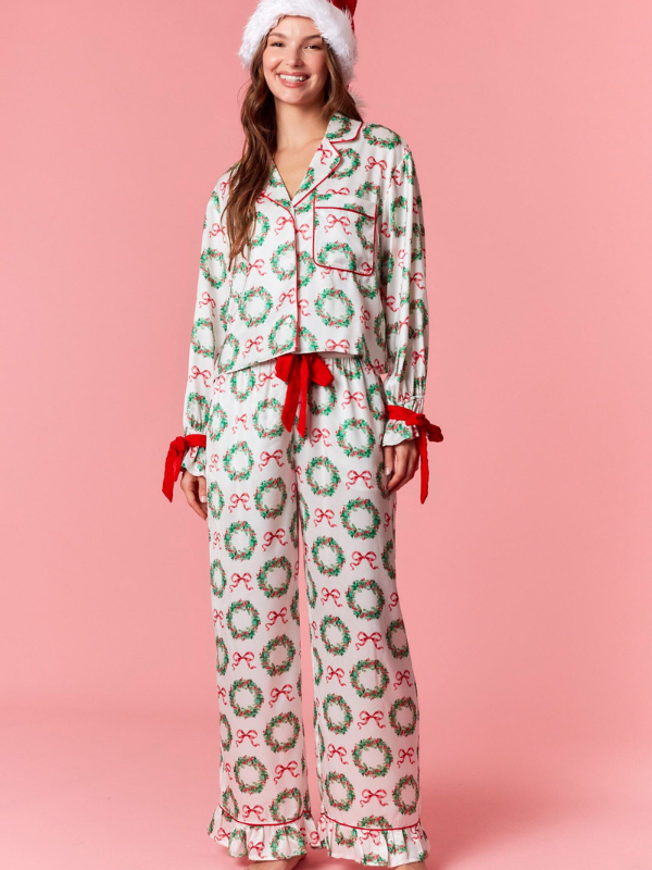 Woman wearing festive pajamas with wreath and bow pattern on a pink background