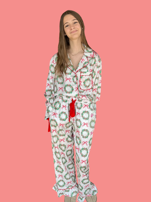 Person wearing a festive pajama set with wreath and bow pattern on a pink background