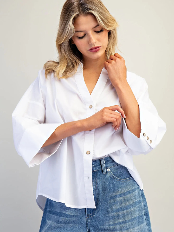 Woman wearing a white blouse with rolled-up sleeves and blue jeans on a plain background