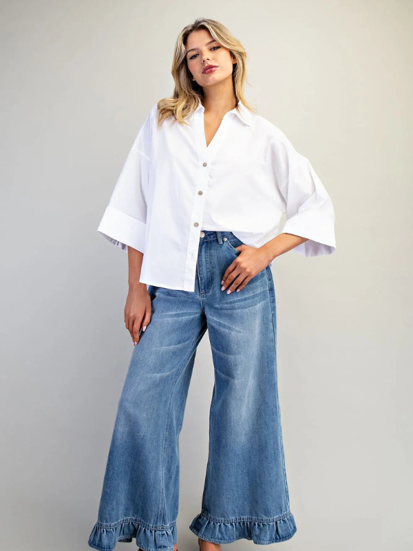 Woman wearing a white blouse and blue jeans with ruffled cuffs on a plain background