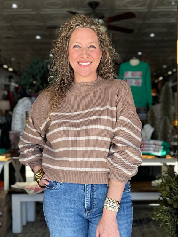 Woman wearing a brown and beige striped sweater and blue jeans in an indoor setting.