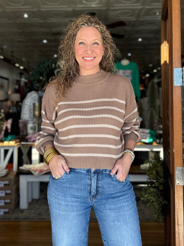 Woman wearing a brown and beige striped sweater and blue jeans in an indoor setting.