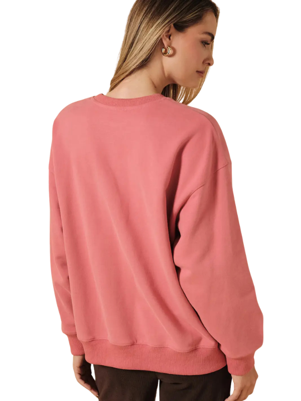 A woman shown from the back wearing a dusty rose crewneck sweatshirt and dark brown pants, photographed against a solid white background.