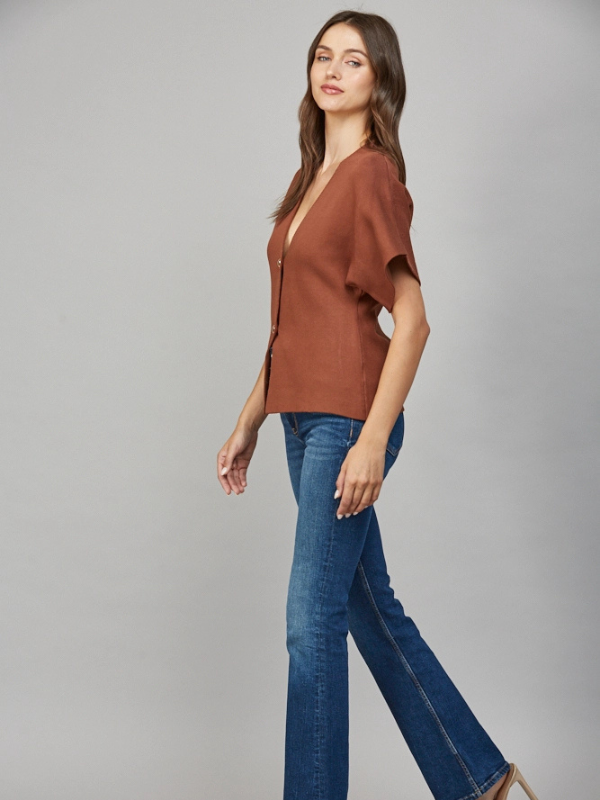 Woman wearing a brown top and blue jeans on a gray background