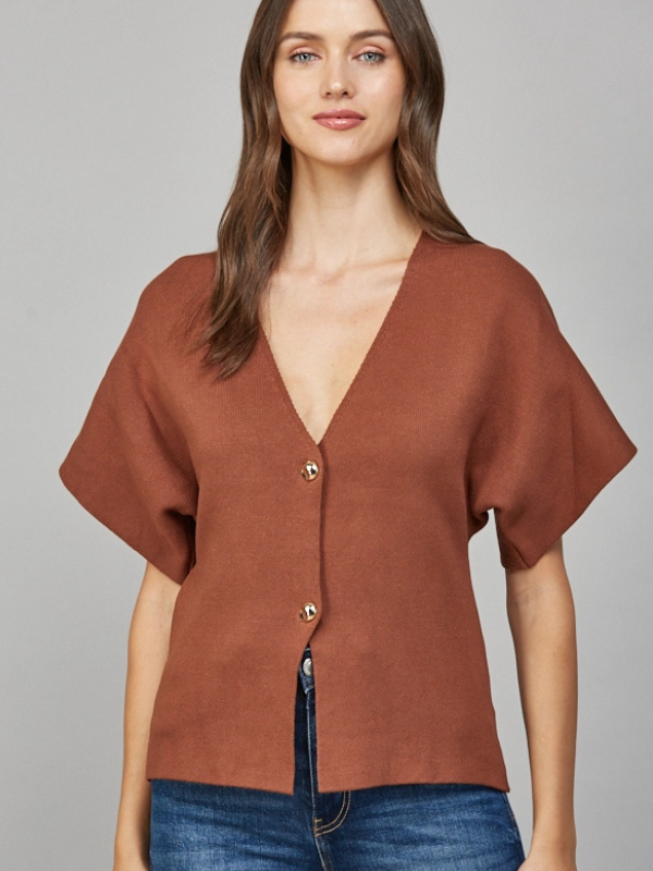 Woman wearing a brown short-sleeve top with buttons on a gray background