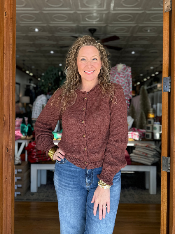 Woman wearing a brown sweater and blue jeans standing in a store.