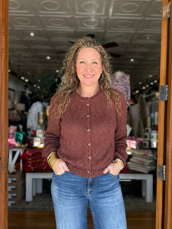 Woman wearing a brown sweater and blue jeans standing inside a store.