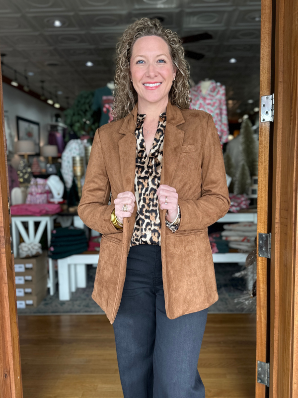 Woman wearing a brown jacket and leopard print top standing in a store.