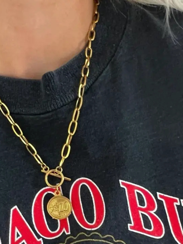 Gold chain necklace with a pendant on a dark shirt with red text