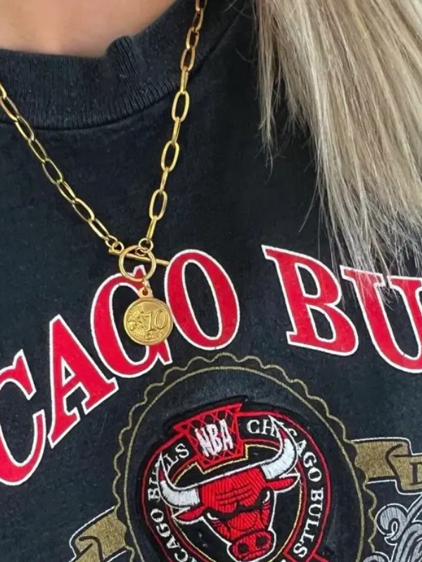 Person wearing a gold necklace with a pendant, standing in front of a Chicago Bulls shirt.