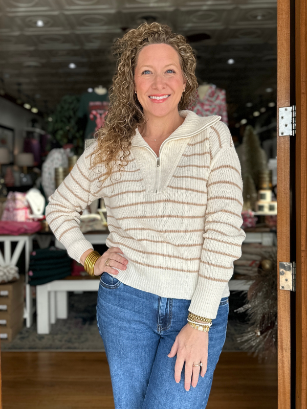 Woman wearing a cream ribbed sweater and blue jeans standing in a store.