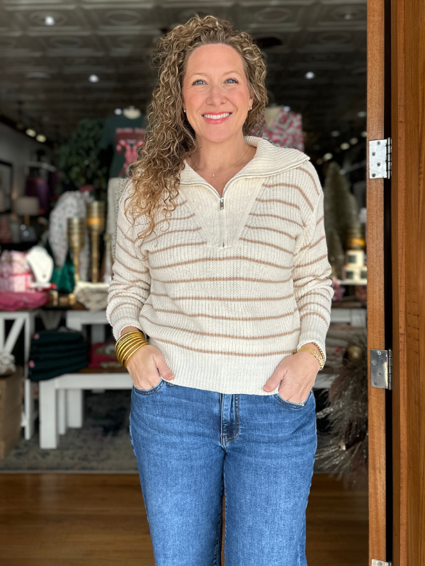 Woman wearing a striped sweater and blue jeans standing indoors.