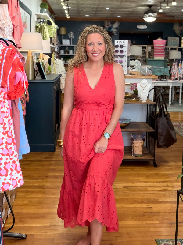 Woman in a red dress standing in a store with various items on shelves and tables.