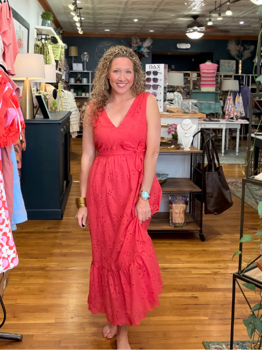 Woman in a red dress standing in a store with various items on shelves and tables.