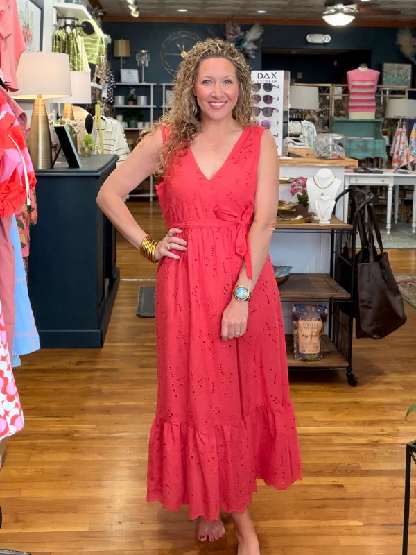 Woman in a red dress standing in a store with various items on shelves in the background.