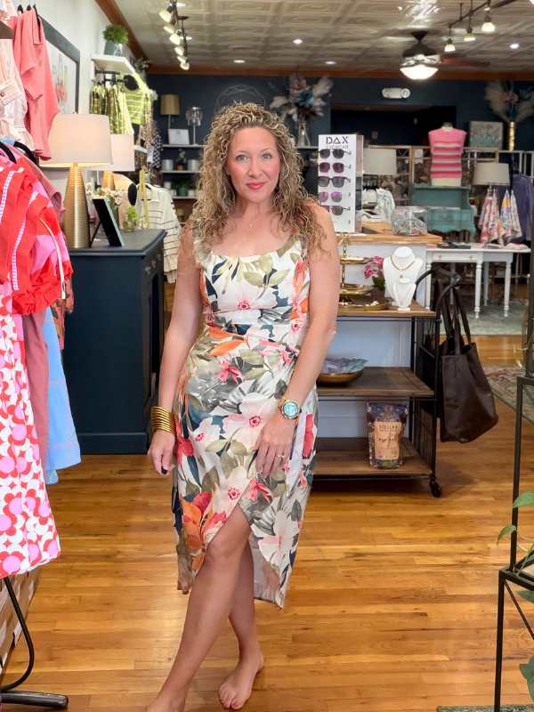 Woman in a floral dress standing in a store with clothing and accessories on display.