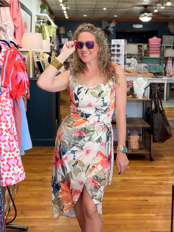 Woman wearing a floral dress and sunglasses in a clothing store.
