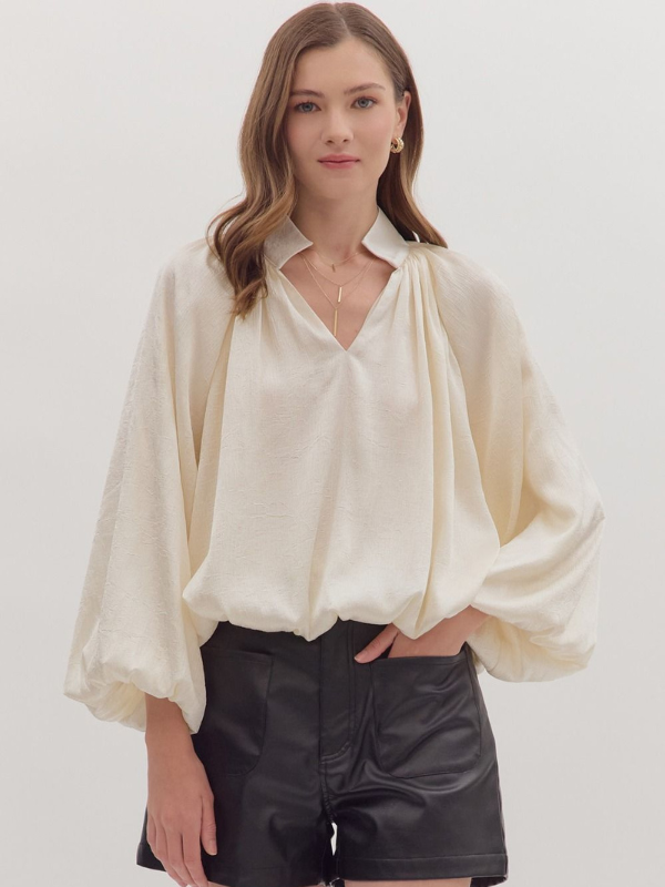 Woman wearing a cream blouse and black pants on a white background