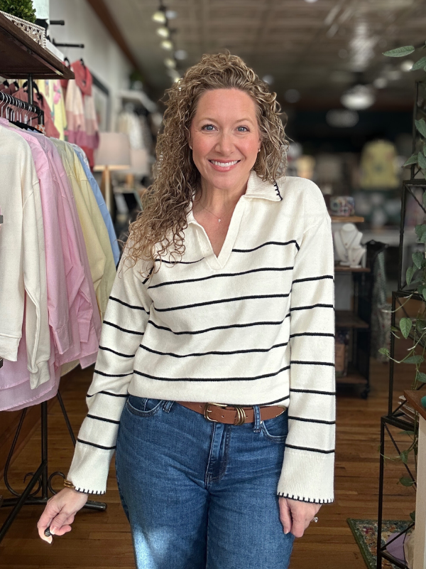 Woman wearing a white sweater with black stripes and blue jeans in a clothing store.