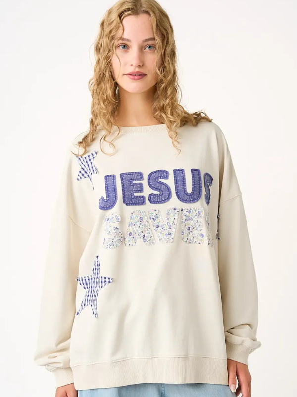 Person wearing a cream sweatshirt with 'Jesus Loves Me' text and star designs.