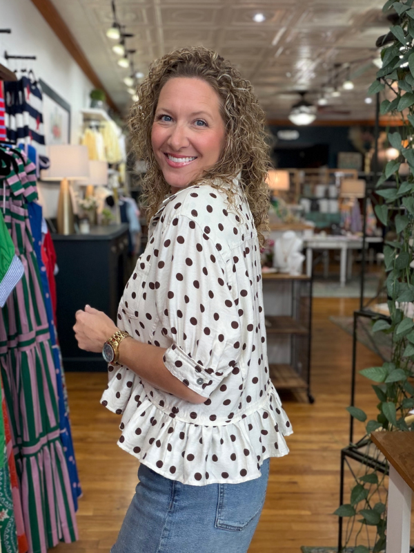 woman wearing a brown and cream polka dot top in a store 