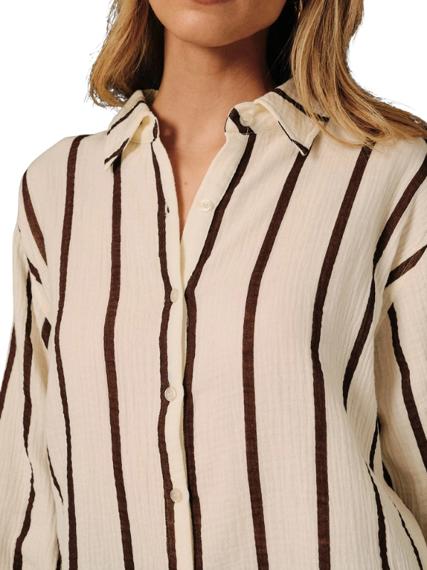 A close-up of a woman wearing a cream-colored crinkled button-up shirt with dark brown vertical stripes.