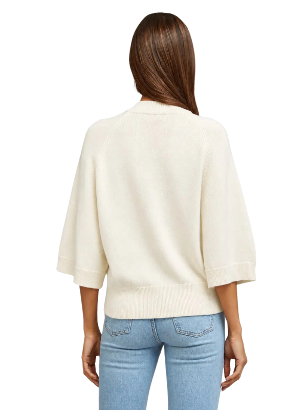 A woman viewed from the back wearing a cream-colored knit sweater with elbow-length sleeves and light blue jeans, set against a plain white background.