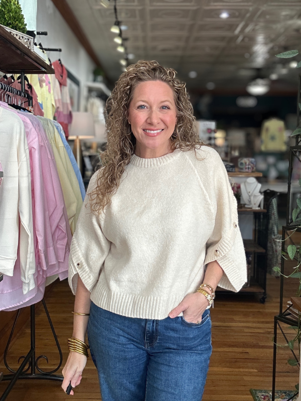 Woman wearing a beige sweater and blue jeans standing in a clothing store.