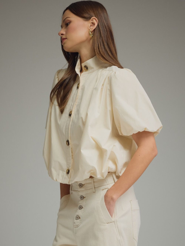 Woman wearing a cream-colored blouse with puffed sleeves against a gray background