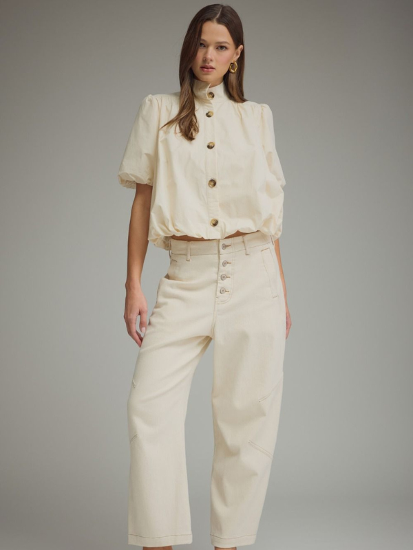 Woman wearing a cream-colored outfit with a matching top and pants on a gray background