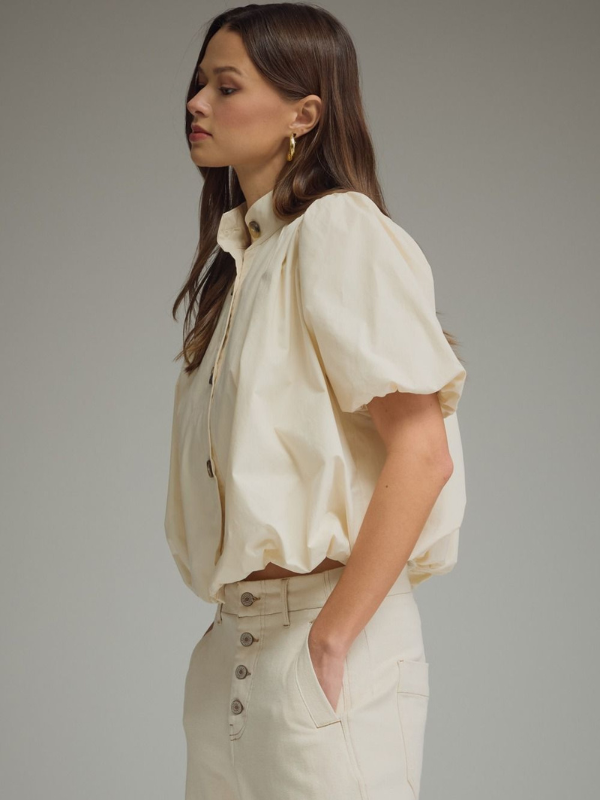 Woman wearing a cream-colored blouse and pants against a neutral background