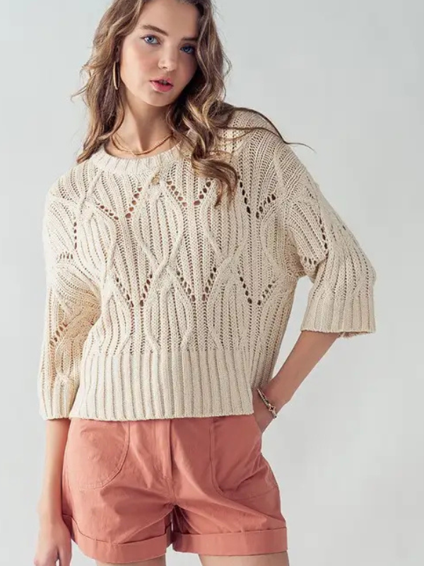 Woman wearing a beige knitted sweater and pink shorts on a white background