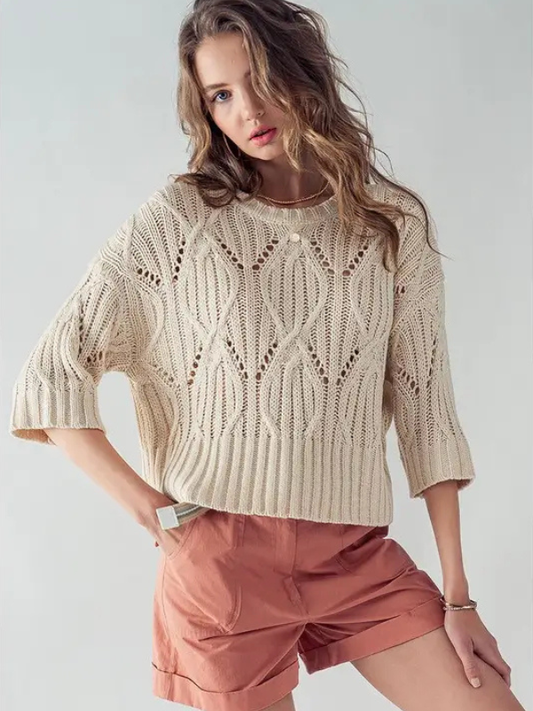 Woman wearing a beige knitted sweater and pink shorts on a light gray background