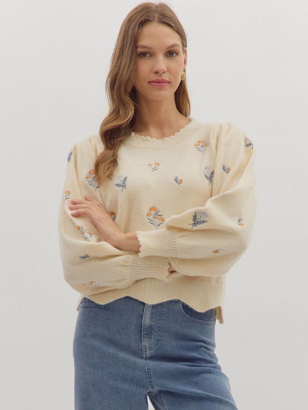 Woman wearing a cream sweater with floral patterns and blue jeans on a white background