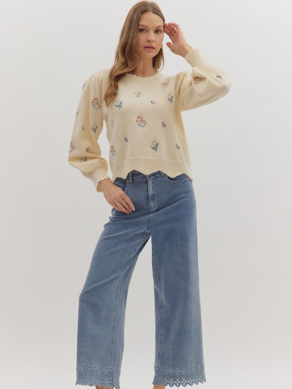 Woman wearing a cream sweater with floral patterns and blue jeans on a white background