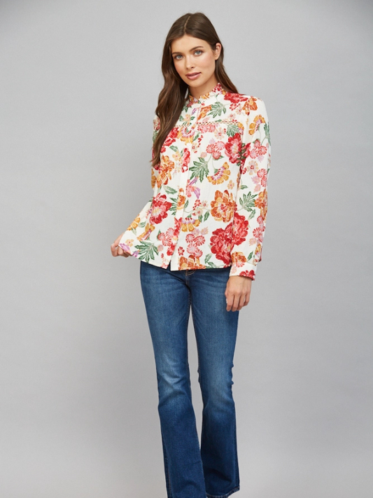 A woman modeling a long-sleeve floral button-up blouse with blue jeans, standing against a solid gray studio background.
