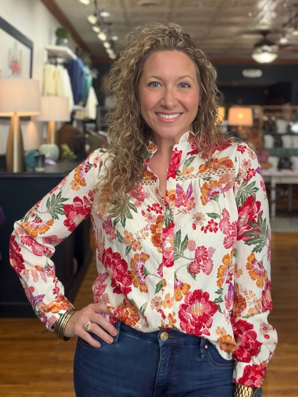 A woman modeling a long-sleeve high-neck blouse with a vibrant multicolor floral print with jeans