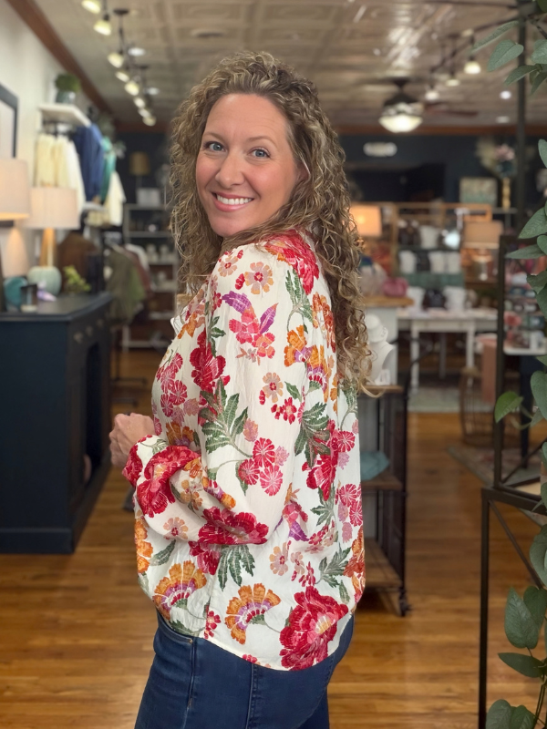 A woman modeling a long-sleeve high-neck blouse with a vibrant multicolor floral print with jeans