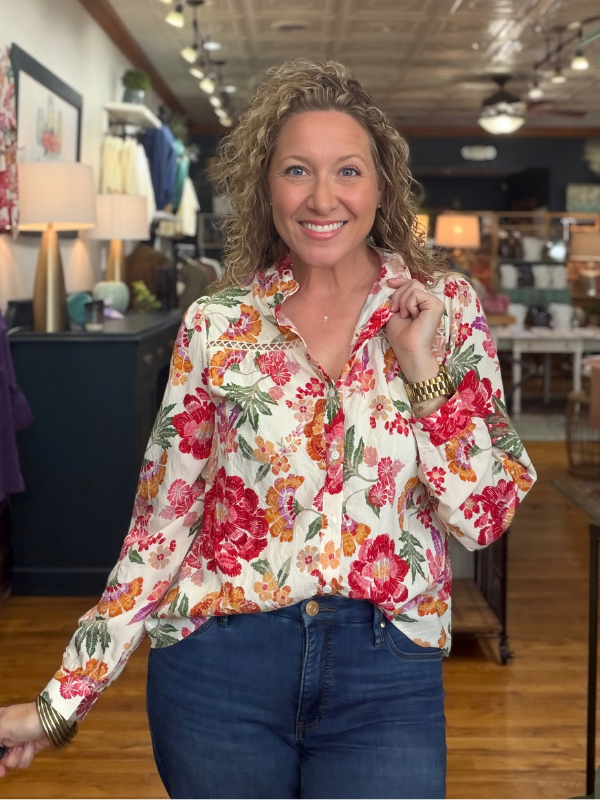 A woman modeling a long-sleeve high-neck blouse with a vibrant multicolor floral print with jeans