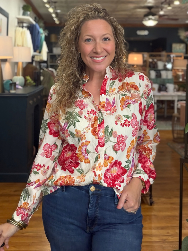 A woman modeling a long-sleeve high-neck blouse with a vibrant multicolor floral print with jeans