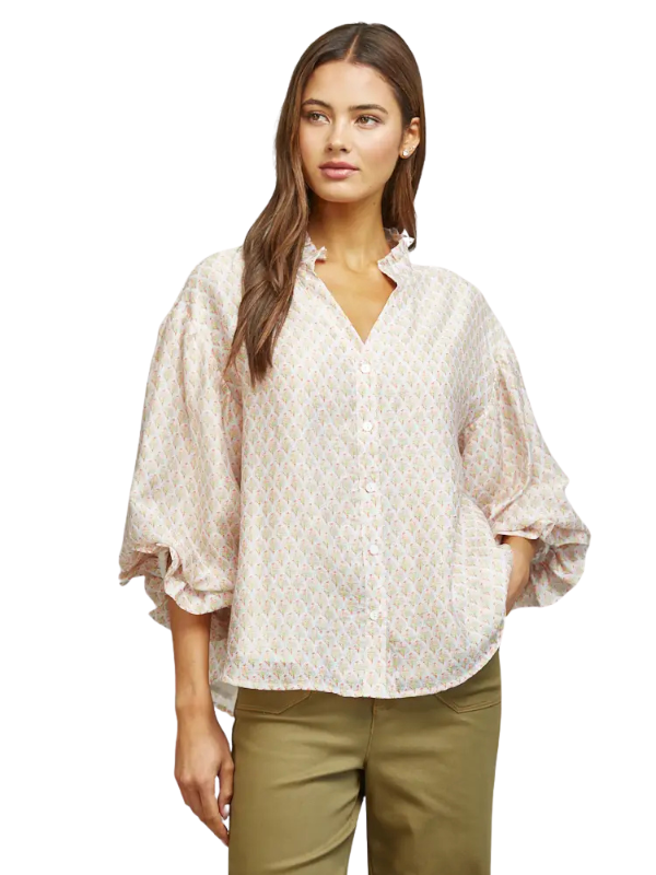 A woman modeling a loose-fitting, short-sleeve button-up blouse with a delicate beige and white geometric pattern, paired with olive green pants, against a plain white background.